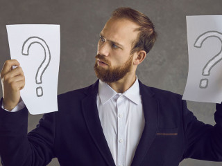 Puzzled businessman holding two question marks asking himself what decision to take
