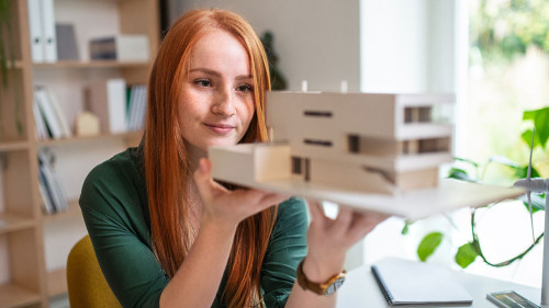 Architect with model of a house sitting at the desk indoors in office.