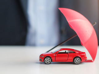 Businessman hand holding umbrella and cover  red car toy on tabl