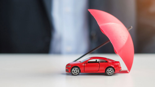 Businessman hand holding umbrella and cover red car toy on tabl