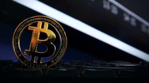 Bitcoin positioned on a computer keyboard with a stock chart in