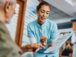 Young nurse assisting senior man in filling paperwork at doctor's office.