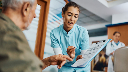 Young nurse assisting senior man in filling paperwork at doctor's office.