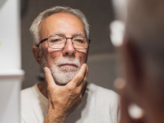 Senior man is looking at his face in bathroom and thinking about