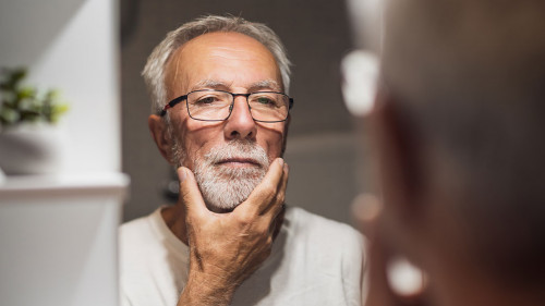 Senior man is looking at his face in bathroom and thinking about