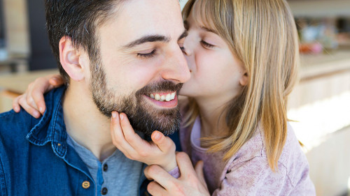 Loving little girl embrace and kissing her father in the kitchen