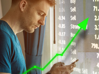 Man on mobile device for trading and stock market upward trend.