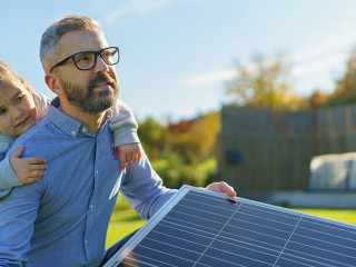 Father with his little daughter catching sun at solar panel,charging at their backyard. Alternative energy, saving resources and sustainable lifestyle concept.