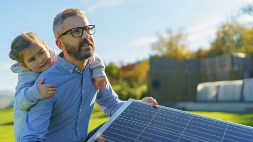 Father with his little daughter catching sun at solar panel,charging at their backyard. Alternative energy, saving resources and sustainable lifestyle concept.