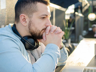 Portrait of unhappy male touching head with hands while looking at notebook computer in cafe