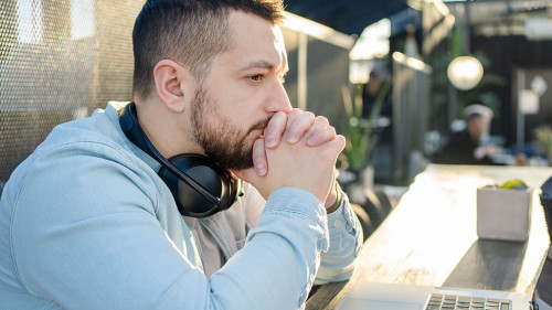 Portrait of unhappy male touching head with hands while looking at notebook computer in cafe