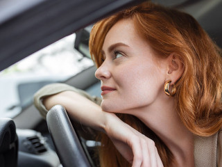 Young Woman Embracing Her New Car. Excited young woman and her new car indoors. Young and cheerful woman enjoying new car hugging steering wheel sitting inside