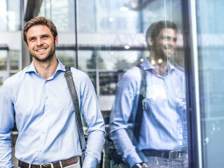 A young businessman with a bag walking in front of a modern building.