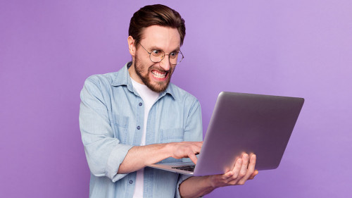 Photo of unhappy angry young man look hold laptop write letter work isolated on purple color background
