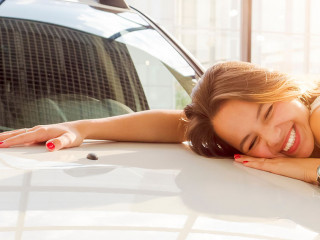 Dream about car. Gorgeous smiling woman hugging lies on the hood of new white car in the dealership.