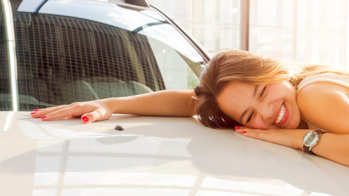 Dream about car. Gorgeous smiling woman hugging lies on the hood of new white car in the dealership.