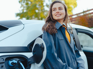 Young woman waiting while her electric car charging in home charging station, sustainable and economic transportation concept.