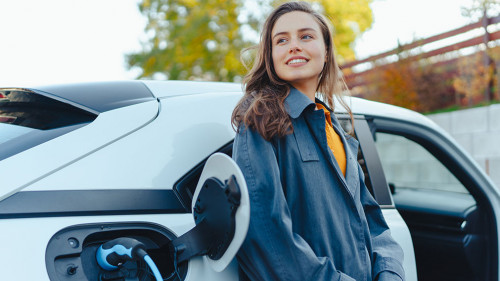Young woman waiting while her electric car charging in home charging station, sustainable and economic transportation concept.