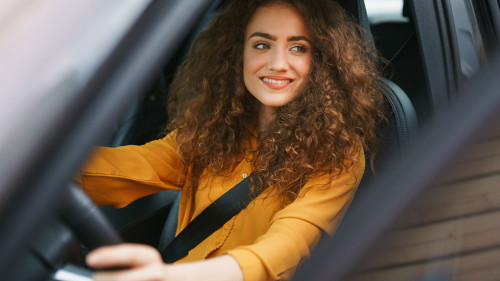 Young woman driving a car in the city. Portrait of a beautiful woman in a car, looking out of the window and smiling.