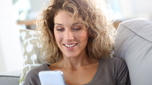 Smiling woman relaxing in sofa with smartphone