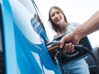Young adult man charging blue electric car