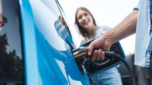 Young adult man charging blue electric car