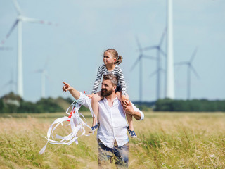 Mature father with small daughter walking on field on wind farm.