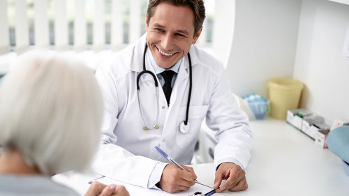 Waist up of cheerful practitioner smiling to the patient while working