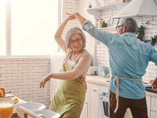Beautiful playful senior couple in aprons dancing and smiling while preparing healthy dinner at home