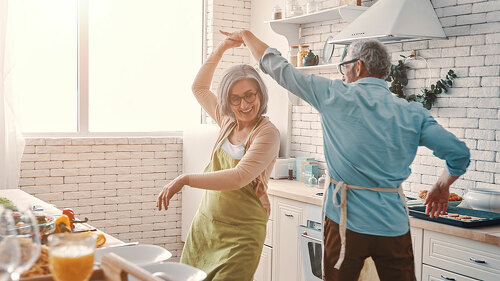 Beautiful playful senior couple in aprons dancing and smiling while preparing healthy dinner at home