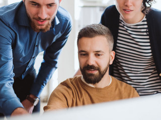 Group of young businesspeople looking at laptop screen in office, discussing issues.