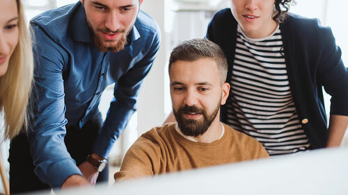 Group of young businesspeople looking at laptop screen in office, discussing issues.