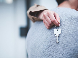 Young woman holding keys hugging husband in front of their new h