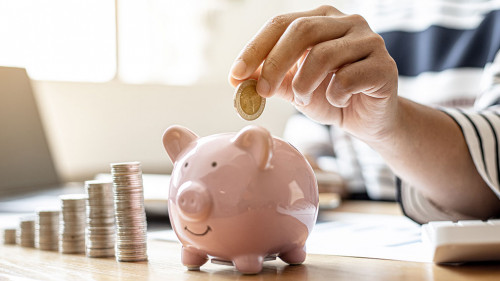 Woman putting a coin into a piggy bank in the shape of a pink pi