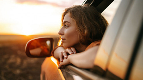 Happy woman outstretches her arms while sticking out the car win
