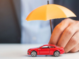 Businessman hand holding umbrella and cover red car toy on tabl