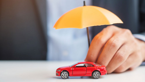 Businessman hand holding umbrella and cover  red car toy on tabl