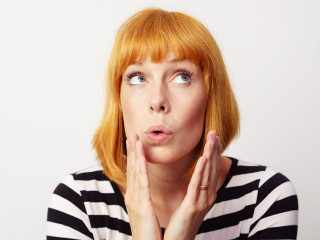Surprised woman with red hair places hands by face