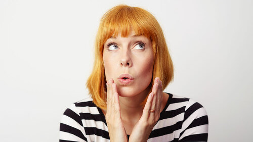 Surprised woman with red hair places hands by face