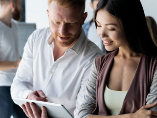 Discussing new business project. Two happy young people smiling and looking at digital tablet while working together
