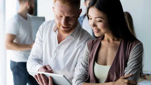 Discussing new business project. Two happy young people smiling and looking at digital tablet while working together