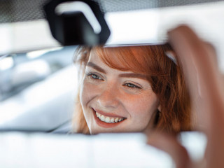 Woman hand adjusting rear view mirror of her car. Happy young woman driver looking adjusting rear view car mirror, making sure line is free visibility is good