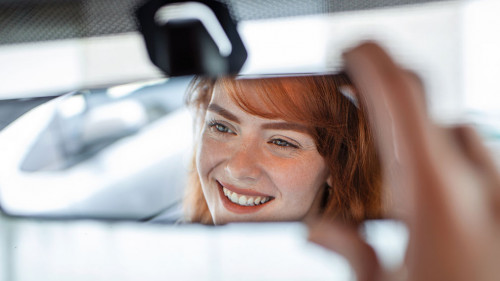 Woman hand adjusting rear view mirror of her car. Happy young woman driver looking adjusting rear view car mirror, making sure line is free visibility is good