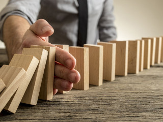 Man stopping domino effect on wooden table