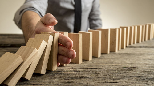 Man stopping domino effect on wooden table