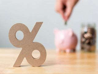 Percentage sign symbol with blurred hand putting money coin in piggy bank