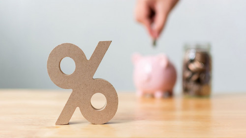 Percentage sign symbol with blurred hand putting money coin in piggy bank