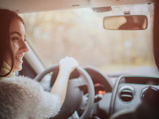Long-haired brunette on the auto background. A female model is wearing a sweater and a scarf. Autumn concept. Autumn forest journey by car