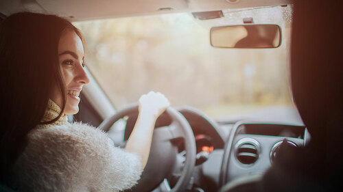 Long-haired brunette on the auto background. A female model is wearing a sweater and a scarf. Autumn concept. Autumn forest journey by car