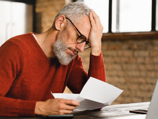 Expensive charges on domestic bills. Loan, debt, bunkruptcy concept. Sad depressed caucasian businessman holding documents, having problems with dismissal at home office